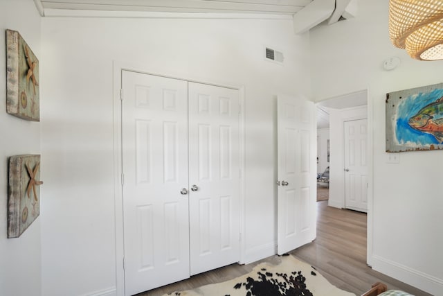 bedroom with hardwood / wood-style floors, vaulted ceiling with beams, and a closet