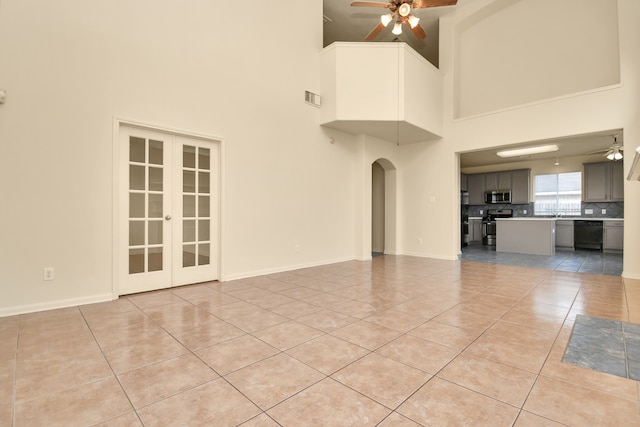 unfurnished living room with a high ceiling, ceiling fan, french doors, and light tile patterned flooring