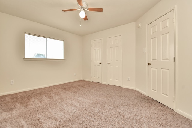 unfurnished bedroom with light carpet, ceiling fan, and multiple closets