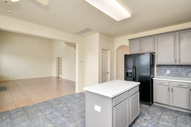 kitchen featuring gray cabinetry, a center island, decorative backsplash, ceiling fan, and black fridge with ice dispenser