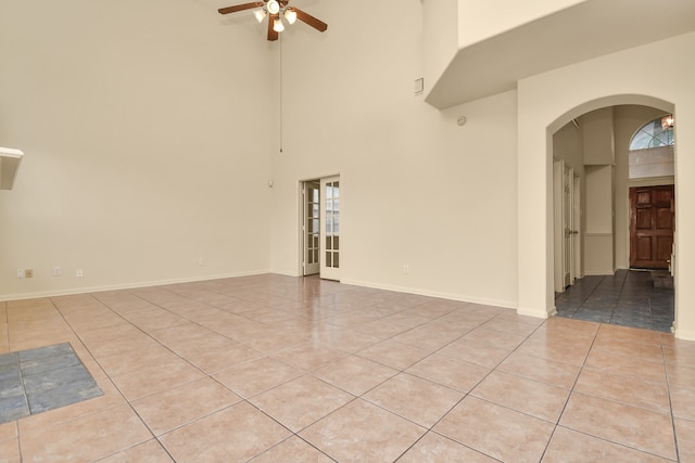 tiled spare room featuring ceiling fan and a towering ceiling