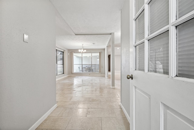 corridor with light tile patterned floors, a textured ceiling, and an inviting chandelier