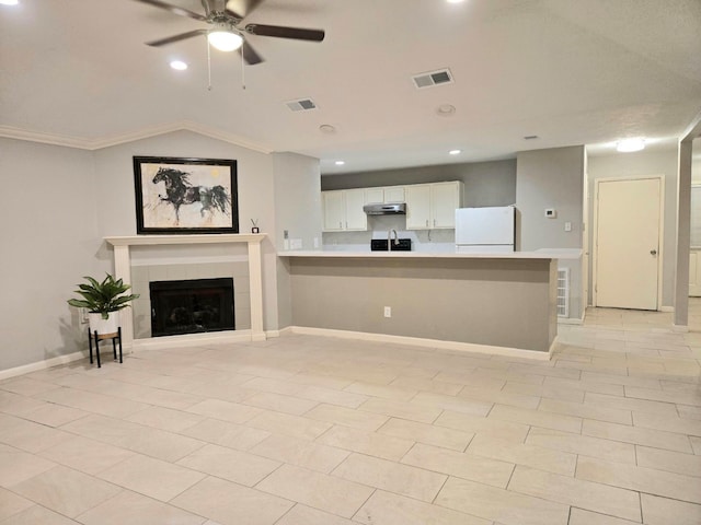 unfurnished living room with ceiling fan, vaulted ceiling, a tiled fireplace, light tile patterned floors, and ornamental molding