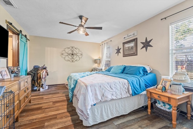 bedroom featuring a barn door, ceiling fan, dark hardwood / wood-style flooring, and a textured ceiling