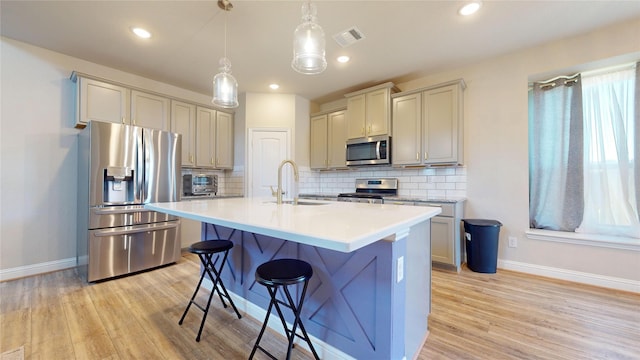 kitchen with sink, an island with sink, pendant lighting, a kitchen bar, and appliances with stainless steel finishes