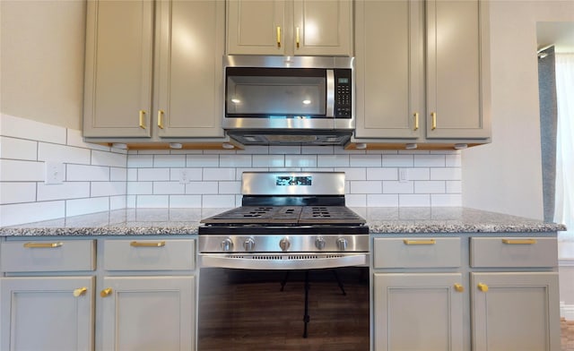 kitchen featuring backsplash, stainless steel appliances, light stone counters, and gray cabinetry