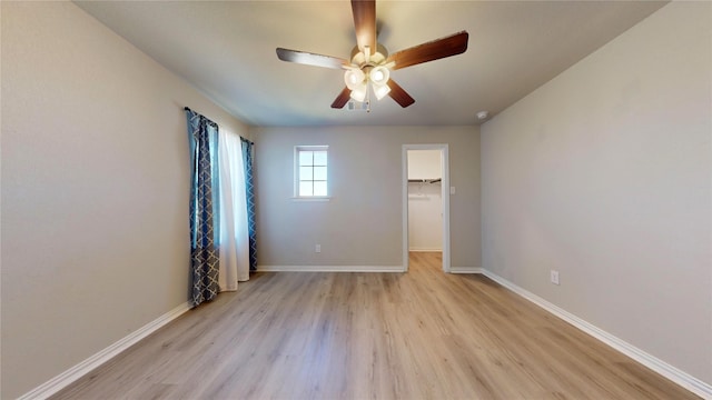 unfurnished bedroom with ceiling fan, a spacious closet, and light wood-type flooring