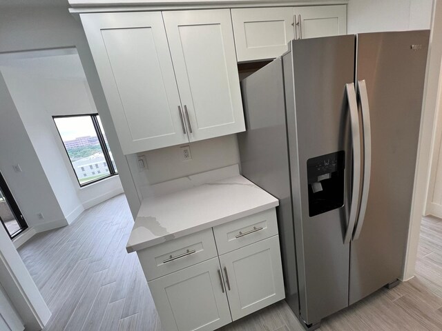 kitchen featuring light stone counters, white cabinets, light wood-type flooring, and stainless steel fridge