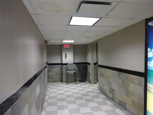 corridor with a paneled ceiling and tile walls