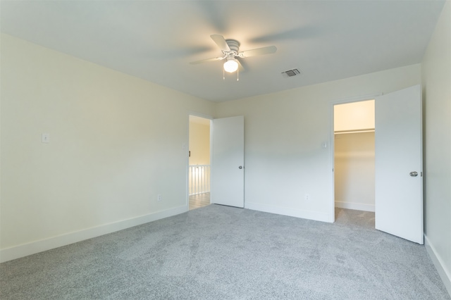 unfurnished bedroom featuring light carpet, a spacious closet, a closet, and ceiling fan