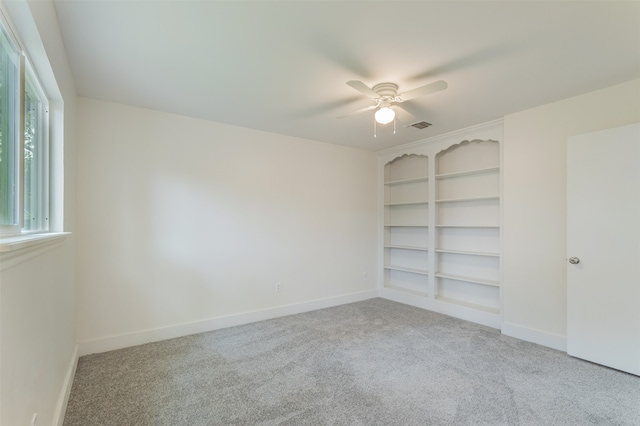 spare room with light carpet, built in shelves, and ceiling fan