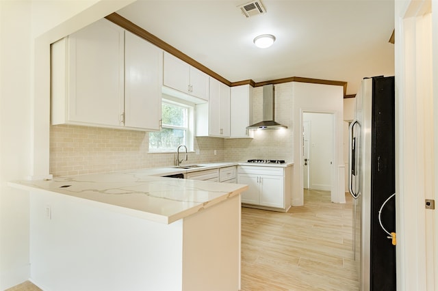 kitchen featuring white cabinets, sink, stainless steel refrigerator with ice dispenser, wall chimney exhaust hood, and kitchen peninsula