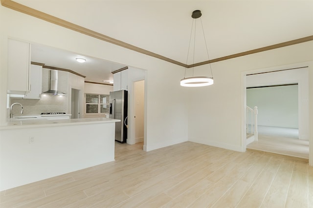 kitchen featuring sink, wall chimney exhaust hood, hanging light fixtures, stainless steel refrigerator with ice dispenser, and white cabinets