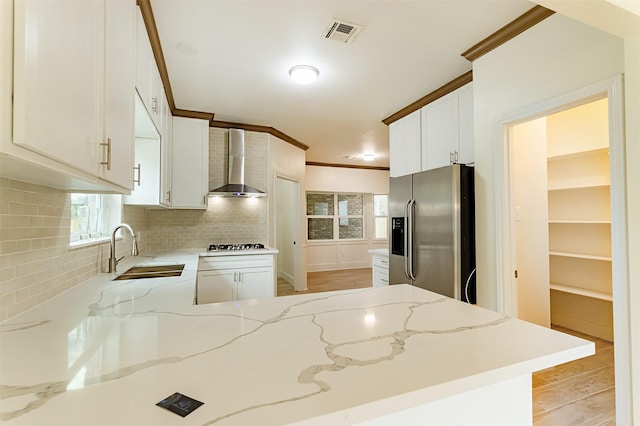 kitchen featuring wall chimney range hood, sink, white cabinets, stainless steel fridge with ice dispenser, and kitchen peninsula