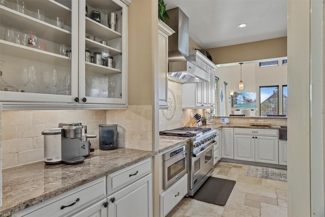 kitchen with light stone countertops, appliances with stainless steel finishes, wall chimney exhaust hood, pendant lighting, and white cabinetry