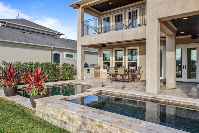 view of pool with a patio area, an in ground hot tub, french doors, and exterior kitchen