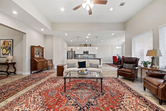 living room with ceiling fan with notable chandelier and light hardwood / wood-style floors