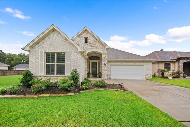 french provincial home with a front yard, driveway, stone siding, and an attached garage
