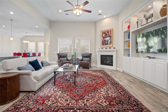 living room with built in features, light hardwood / wood-style floors, and ceiling fan with notable chandelier