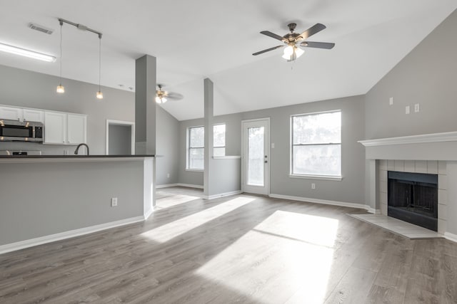 unfurnished living room with ceiling fan, sink, light hardwood / wood-style flooring, high vaulted ceiling, and a fireplace