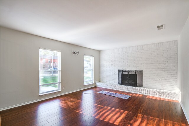 unfurnished living room featuring dark wood-type flooring and a brick fireplace