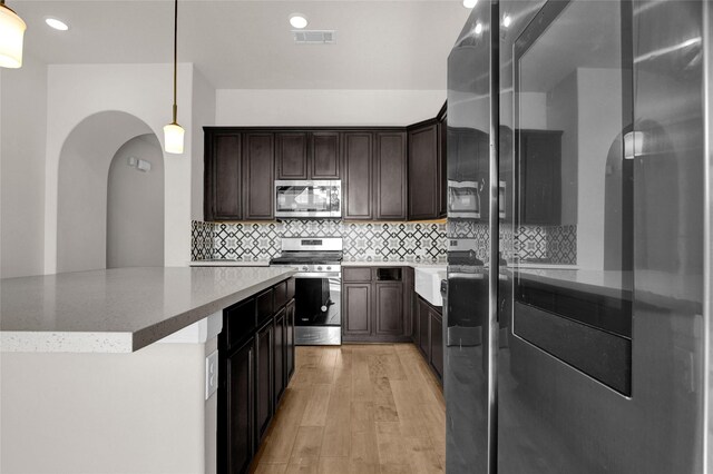 kitchen featuring hanging light fixtures, light hardwood / wood-style floors, decorative backsplash, dark brown cabinets, and appliances with stainless steel finishes