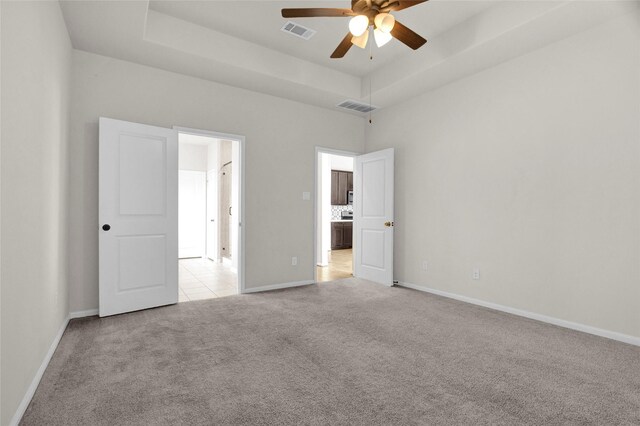 unfurnished bedroom featuring a tray ceiling, ceiling fan, and light colored carpet