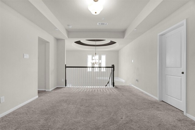 corridor featuring carpet flooring, a chandelier, and a tray ceiling