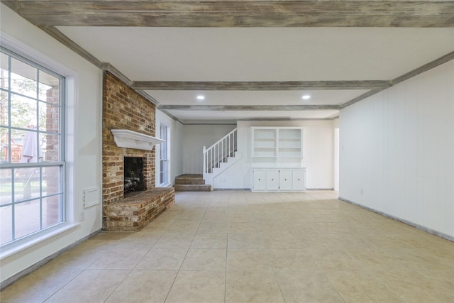 unfurnished living room featuring beam ceiling, light tile patterned floors, ornamental molding, and a brick fireplace