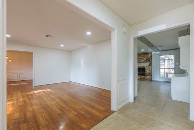 spare room with a brick fireplace, crown molding, and light hardwood / wood-style flooring