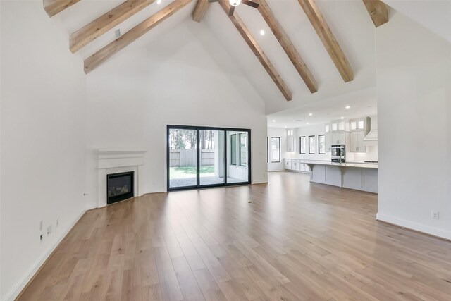 12926 Whitewater Way, Conroe, TX 77302 - unfurnished living room with high vaulted ceiling, beam ceiling, a ceiling fan, a glass covered fireplace, and light wood-style flooring
