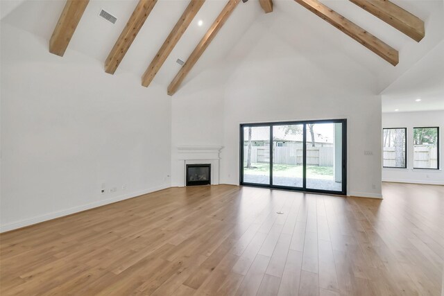 12926 Whitewater Way, Conroe, TX 77302 - unfurnished living room with high vaulted ceiling, beam ceiling, recessed lighting, a glass covered fireplace, and light wood-style flooring