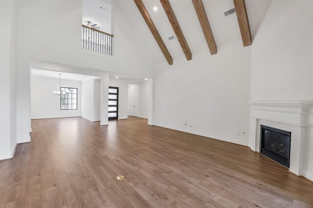 12926 Whitewater Way, Conroe, TX 77302 - unfurnished living room with a chandelier, a glass covered fireplace, high vaulted ceiling, beam ceiling, and wood finished floors