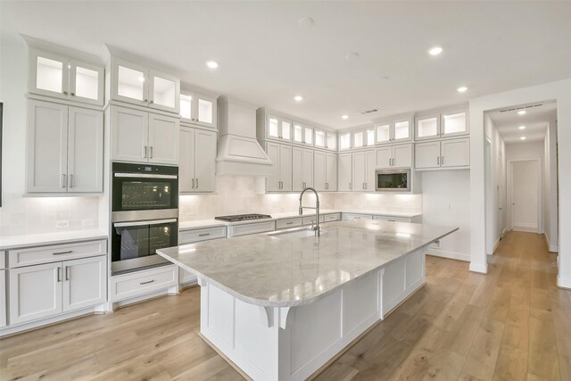 12926 Whitewater Way, Conroe, TX 77302 - kitchen with stainless steel appliances, custom range hood, backsplash, white cabinetry, and a kitchen island with sink