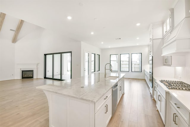 12926 Whitewater Way, Conroe, TX 77302 - kitchen featuring custom range hood, stainless steel appliances, light wood-style floors, a spacious island, and white cabinetry