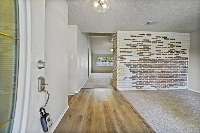 hallway featuring brick wall, light hardwood / wood-style floors, and a textured ceiling