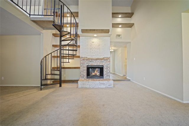 unfurnished living room featuring carpet floors, a towering ceiling, and a brick fireplace