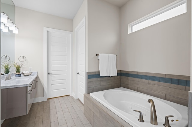 bathroom with hardwood / wood-style floors, vanity, and tiled tub