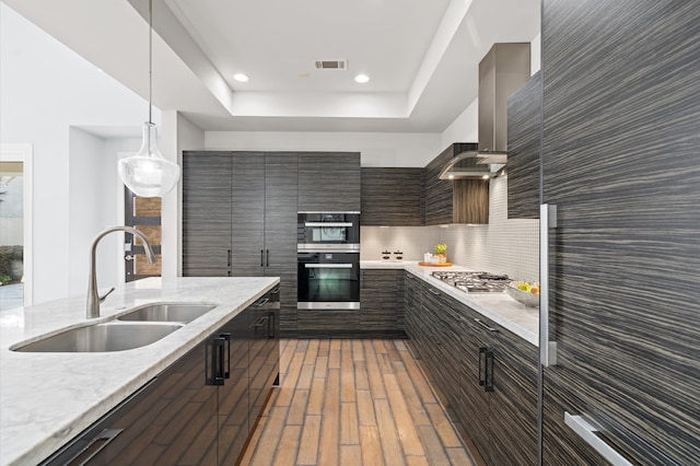 kitchen with appliances with stainless steel finishes, tasteful backsplash, wall chimney range hood, sink, and pendant lighting