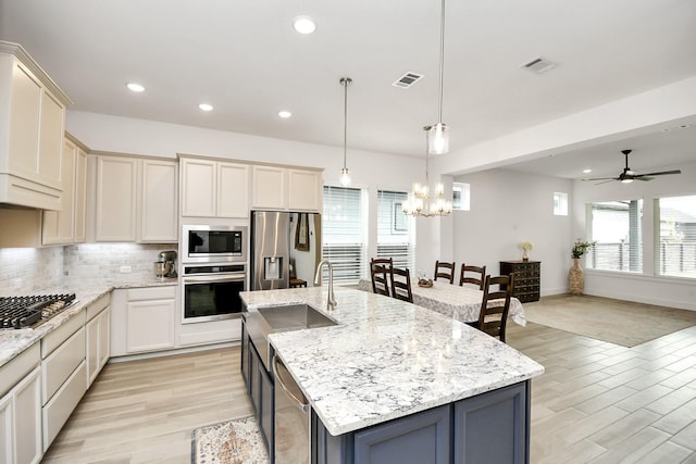 kitchen with hanging light fixtures, appliances with stainless steel finishes, light hardwood / wood-style flooring, and a kitchen island with sink