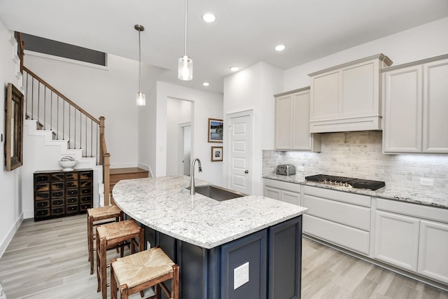 kitchen with sink, gas stovetop, light stone countertops, an island with sink, and light hardwood / wood-style floors