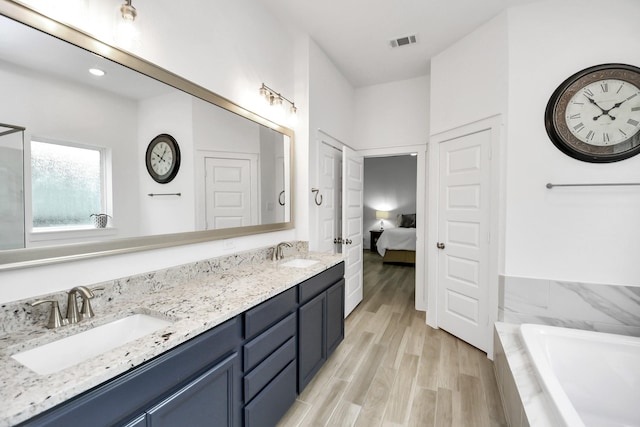 bathroom featuring wood-type flooring, vanity, and tiled tub