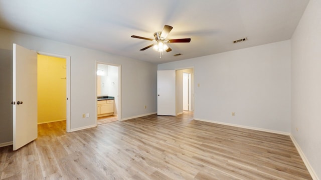 unfurnished bedroom with light wood-type flooring, a spacious closet, ensuite bath, and ceiling fan