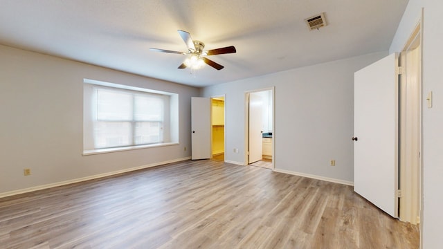 unfurnished bedroom featuring ceiling fan, a spacious closet, light wood-type flooring, connected bathroom, and a closet