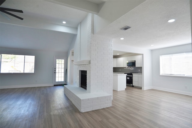 unfurnished living room featuring ceiling fan, plenty of natural light, lofted ceiling with beams, and light wood-type flooring