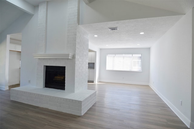 unfurnished living room with hardwood / wood-style flooring, lofted ceiling, a textured ceiling, and a brick fireplace