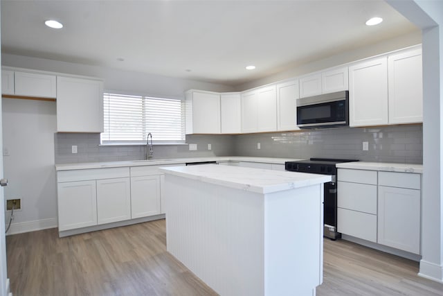 kitchen featuring range with electric cooktop, white cabinetry, a kitchen island, and sink