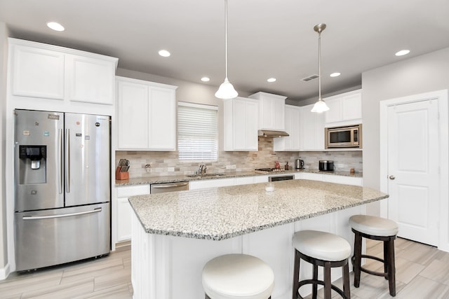 kitchen with a center island, sink, stainless steel appliances, decorative light fixtures, and white cabinets