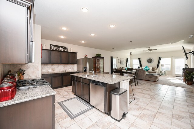 kitchen with appliances with stainless steel finishes, light stone counters, ceiling fan, sink, and an island with sink