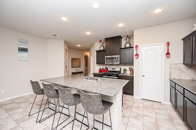 kitchen with sink, stainless steel appliances, tasteful backsplash, and an island with sink